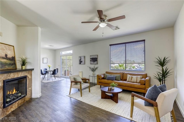 9966 Mystic Moss St, Las Vegas, NV 89183 - living area featuring visible vents, a lit fireplace, baseboards, dark wood finished floors, and a ceiling fan