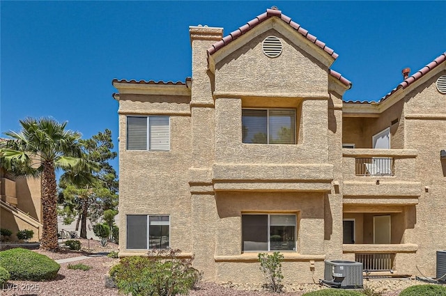 back of property with stucco siding, a tiled roof, central AC unit, and a balcony