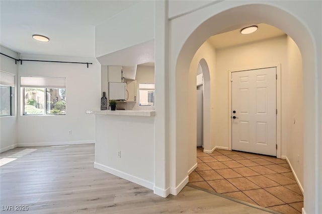foyer entrance with light wood-type flooring, arched walkways, and baseboards