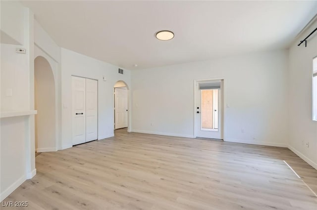 empty room with baseboards, visible vents, arched walkways, and light wood-style floors