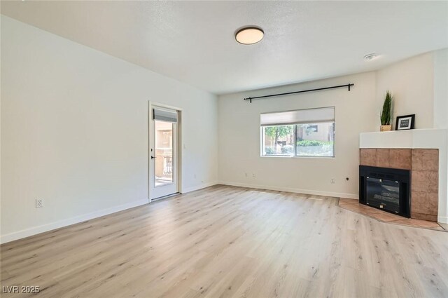 unfurnished living room featuring a tile fireplace, light wood-style flooring, and baseboards
