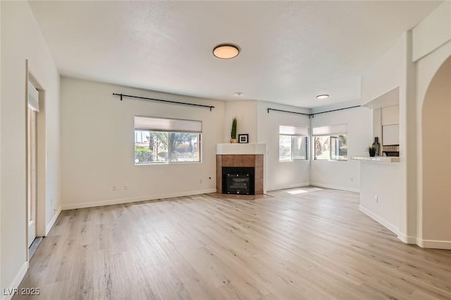 unfurnished living room with light wood-type flooring, a tile fireplace, baseboards, and plenty of natural light