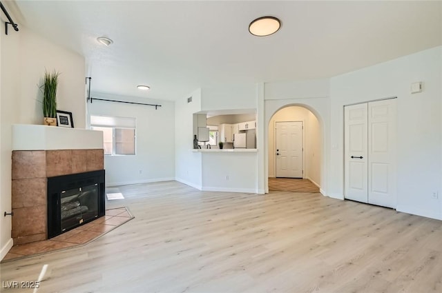 unfurnished living room with baseboards, light wood finished floors, and arched walkways