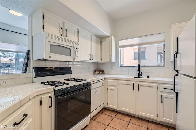 kitchen with tasteful backsplash, white appliances, white cabinets, a sink, and tile countertops