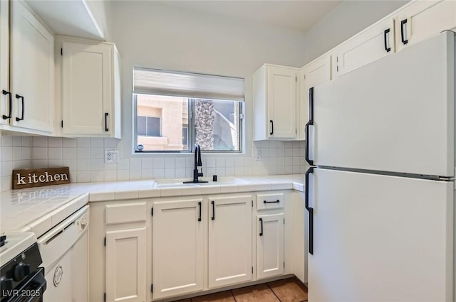 kitchen featuring freestanding refrigerator, tile counters, backsplash, a sink, and white cabinetry
