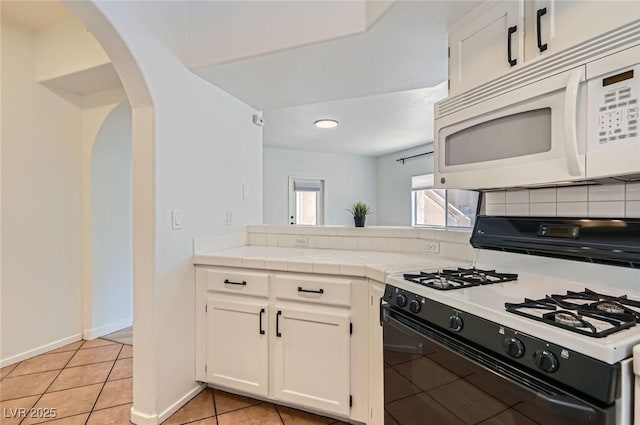 kitchen featuring range with gas stovetop, white cabinetry, decorative backsplash, arched walkways, and white microwave