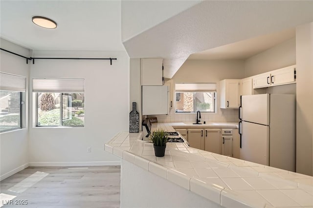 kitchen featuring light wood-style flooring, a sink, tile counters, freestanding refrigerator, and backsplash