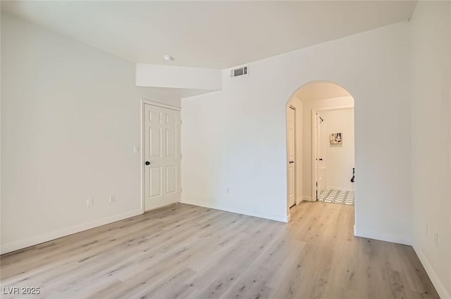 spare room featuring baseboards, visible vents, arched walkways, and light wood-style floors