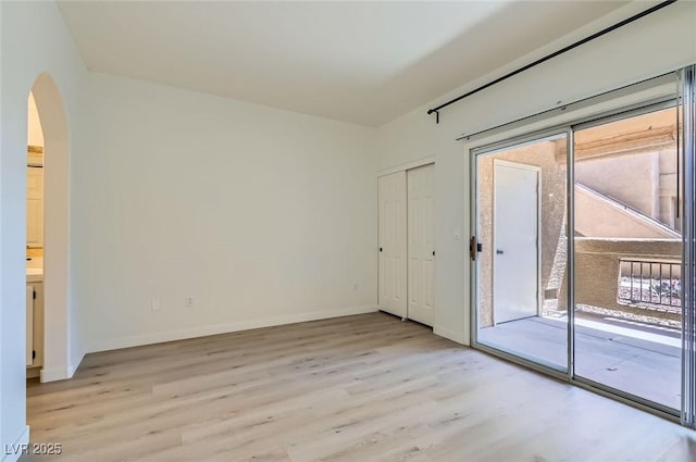 unfurnished room featuring baseboards, arched walkways, and light wood-style floors