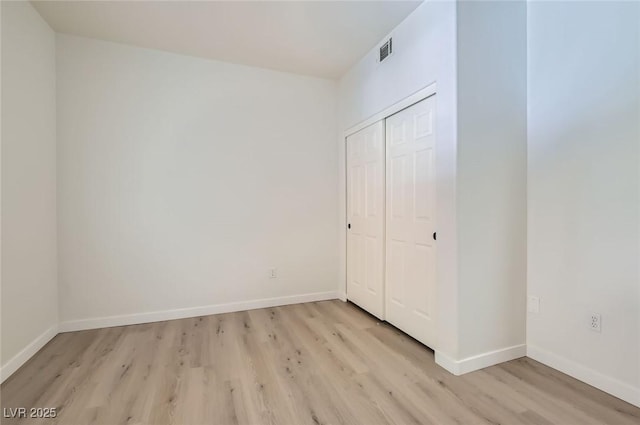 unfurnished bedroom featuring baseboards, visible vents, a closet, and light wood finished floors