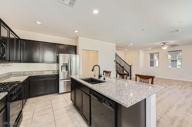 kitchen featuring black appliances, a sink, light stone countertops, a center island with sink, and open floor plan