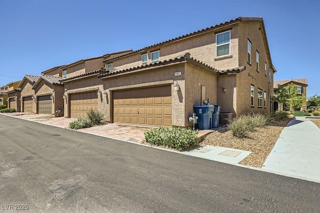 townhome / multi-family property with stucco siding, a tiled roof, and a garage