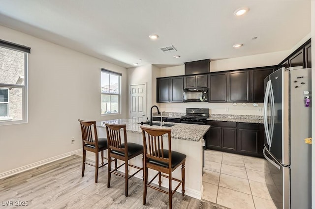 kitchen featuring black appliances, a sink, light stone countertops, a kitchen island with sink, and a kitchen breakfast bar