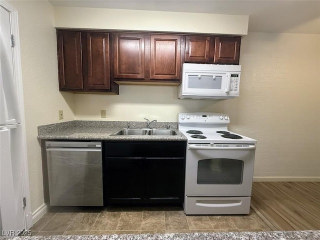kitchen with dark brown cabinetry, white appliances, baseboards, and a sink