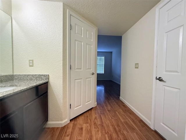 corridor with a textured ceiling, a sink, light wood-style floors, a textured wall, and baseboards