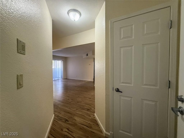 corridor with dark wood finished floors, baseboards, visible vents, and a textured wall