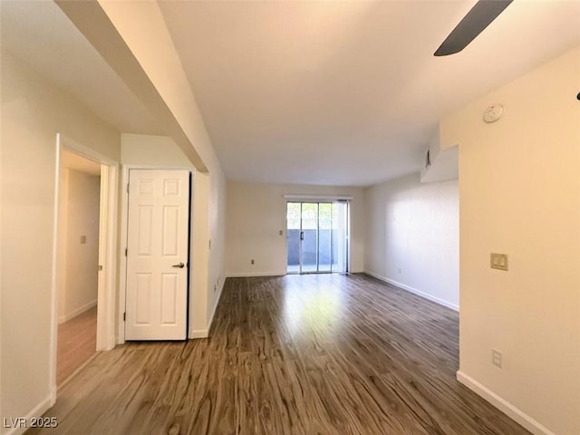 empty room with dark wood-type flooring, a ceiling fan, and baseboards