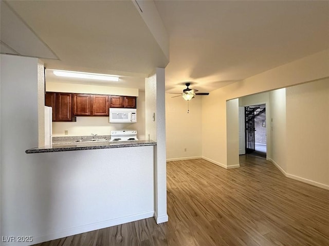 kitchen with a sink, baseboards, wood finished floors, white appliances, and a ceiling fan