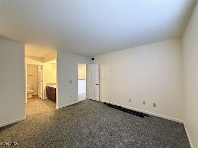 unfurnished bedroom with baseboards, dark colored carpet, visible vents, and ensuite bathroom