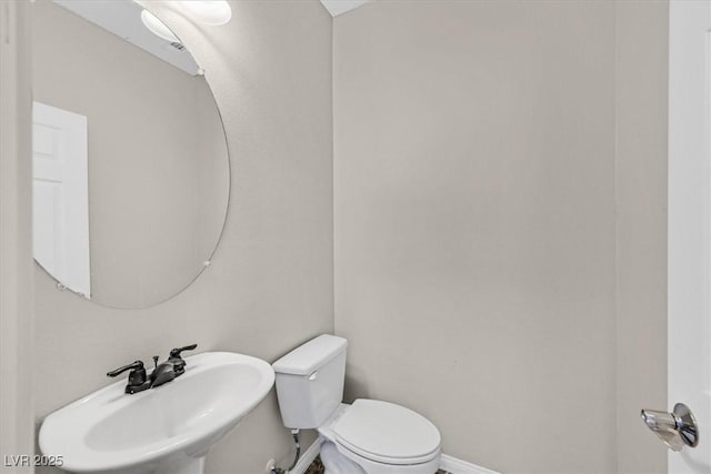 half bath with baseboards, toilet, and a sink