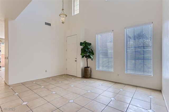 spare room featuring visible vents, light tile patterned floors, and a towering ceiling