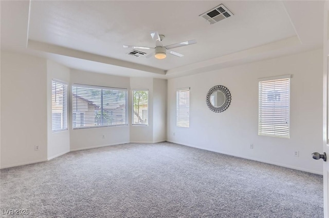 carpeted empty room with baseboards, visible vents, a raised ceiling, and a ceiling fan