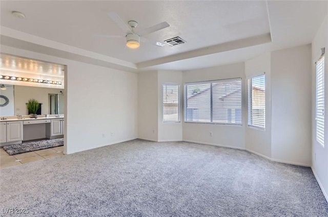 interior space featuring a tray ceiling, visible vents, baseboards, light colored carpet, and ensuite bathroom
