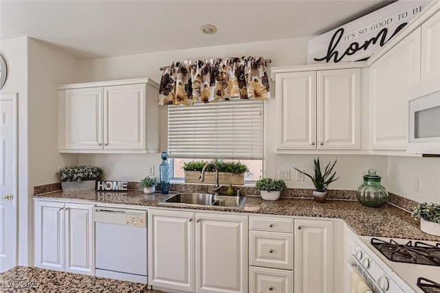 kitchen with dark stone counters, a sink, white cabinets, and white appliances