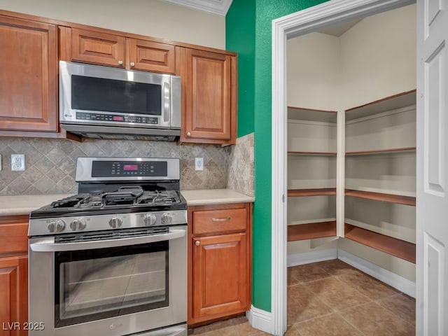 8728 Tom Noon Ave Unit 103, Las Vegas, NV 89178 - kitchen with brown cabinetry, crown molding, backsplash, light countertops, and appliances with stainless steel finishes