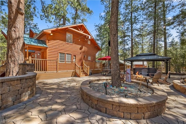 rear view of property featuring a gazebo, a fire pit, faux log siding, and a patio