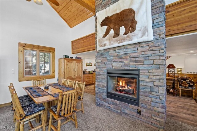 carpeted dining area featuring beamed ceiling, a stone fireplace, high vaulted ceiling, wood ceiling, and a ceiling fan