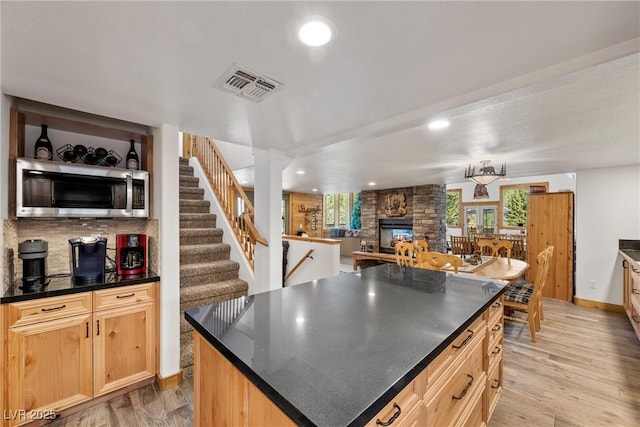 kitchen with visible vents, dark countertops, a fireplace, light wood-type flooring, and stainless steel microwave
