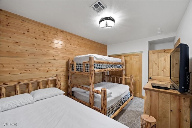carpeted bedroom featuring wood walls, visible vents, and a closet