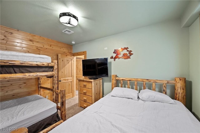 carpeted bedroom featuring wooden walls and visible vents