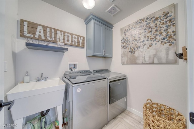 clothes washing area with separate washer and dryer, cabinet space, a sink, baseboards, and visible vents
