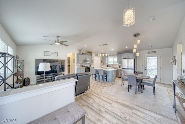 living room featuring light wood-type flooring, visible vents, ceiling fan with notable chandelier, and lofted ceiling