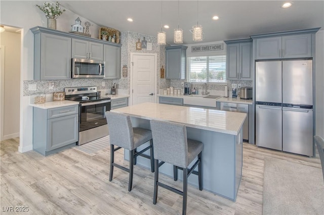 kitchen featuring a sink, light wood-style floors, tasteful backsplash, gray cabinetry, and appliances with stainless steel finishes