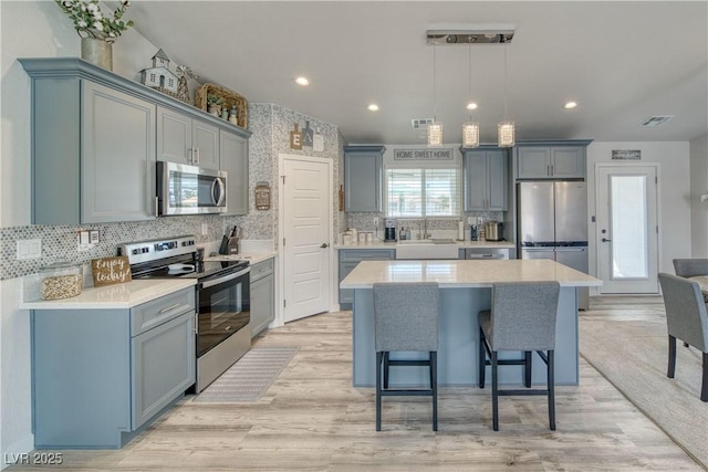 kitchen featuring light wood-style flooring, decorative backsplash, stainless steel appliances, gray cabinetry, and visible vents