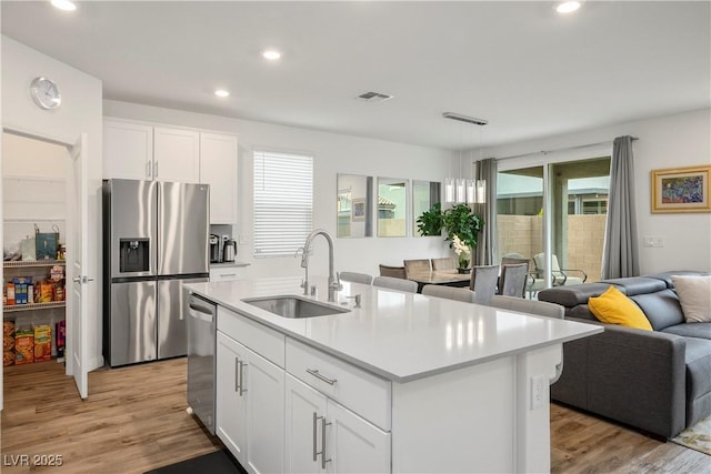 kitchen featuring light wood-style floors, open floor plan, white cabinets, a sink, and stainless steel appliances