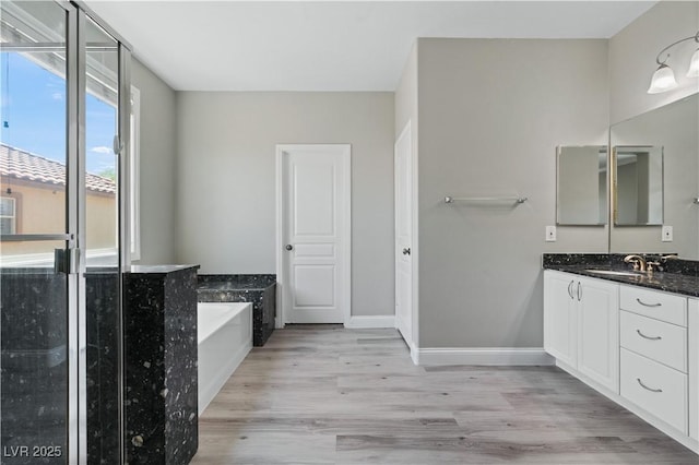 full bathroom with baseboards, wood finished floors, a garden tub, and vanity