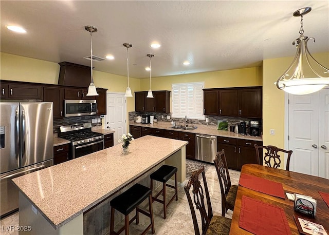 kitchen featuring tasteful backsplash, a sink, appliances with stainless steel finishes, a kitchen island, and dark brown cabinetry