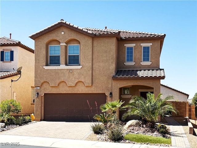 mediterranean / spanish house with stucco siding, a tiled roof, and an attached garage