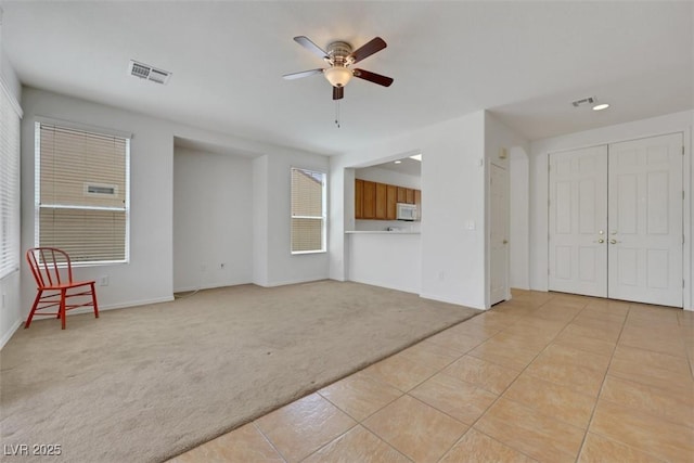 unfurnished living room featuring light tile patterned floors, visible vents, a ceiling fan, and light carpet