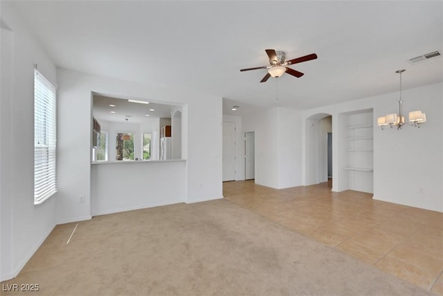 unfurnished living room with visible vents, arched walkways, built in features, tile patterned flooring, and ceiling fan with notable chandelier
