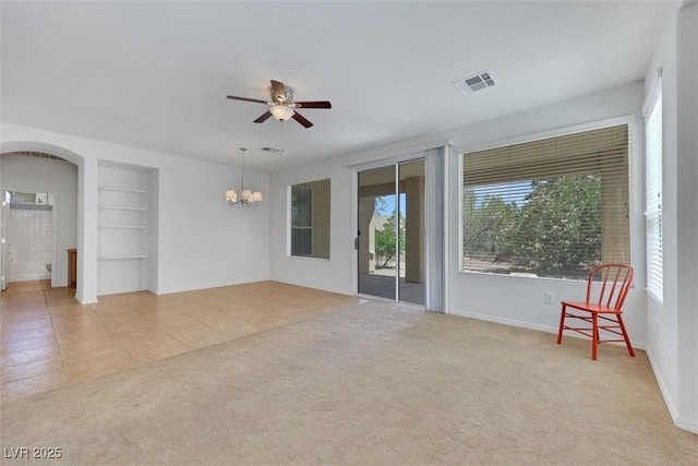 interior space featuring carpet flooring, visible vents, arched walkways, built in features, and ceiling fan with notable chandelier