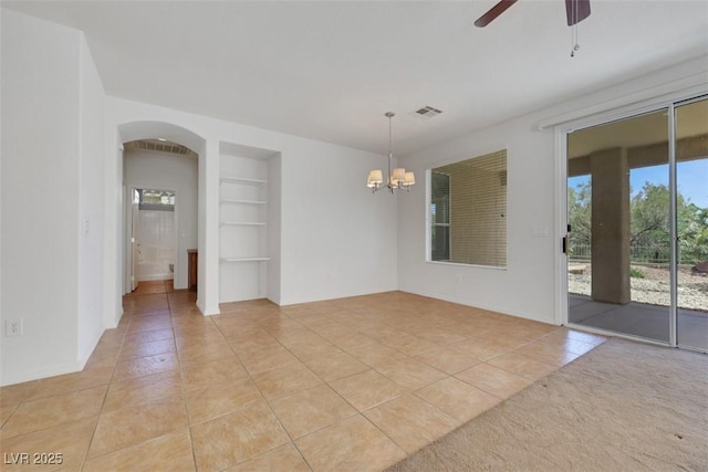 unfurnished room featuring arched walkways, light tile patterned floors, built in features, ceiling fan with notable chandelier, and visible vents