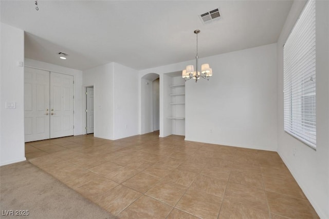 spare room with a chandelier, light tile patterned floors, built in features, visible vents, and arched walkways