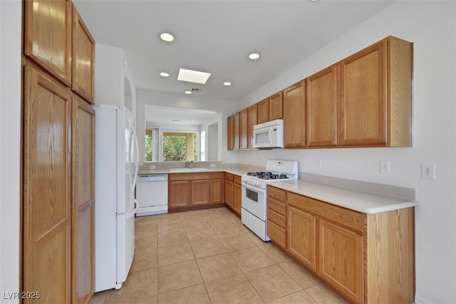 kitchen featuring a skylight, white appliances, light countertops, a sink, and light tile patterned flooring
