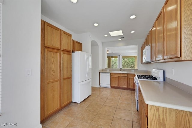 kitchen with a skylight, white appliances, light tile patterned floors, light countertops, and a sink