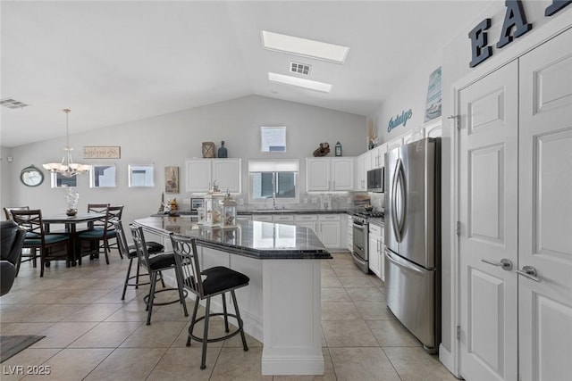 5205 Molveno Ct, Las Vegas, NV 89130 - kitchen with stainless steel appliances, a breakfast bar area, white cabinets, vaulted ceiling, and light tile patterned floors